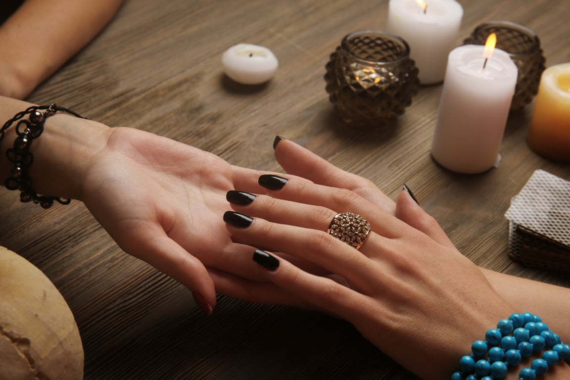 two hands with black nail polish on a wooden table