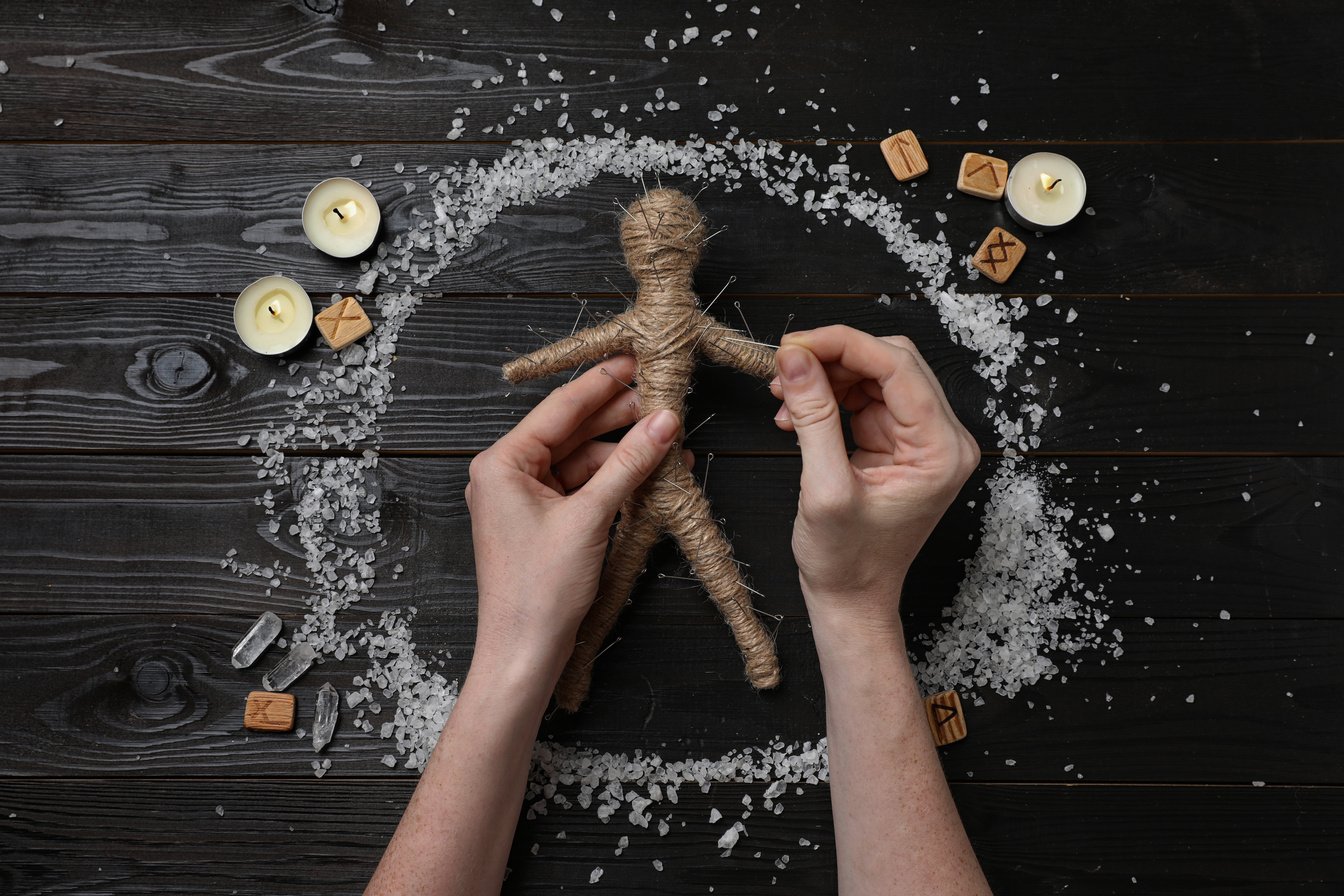 Woman Stabbing Voodoo Doll with Pins at Wooden Table, Top View